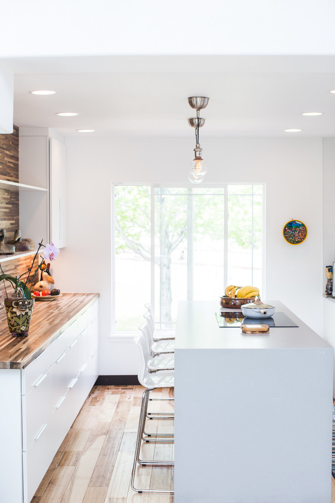 Photo of a medium sized contemporary u-shaped kitchen/diner in Denver with a submerged sink, flat-panel cabinets, white cabinets, engineered stone countertops, white splashback, ceramic splashback, black appliances, light hardwood flooring, an island, brown floors and grey worktops.