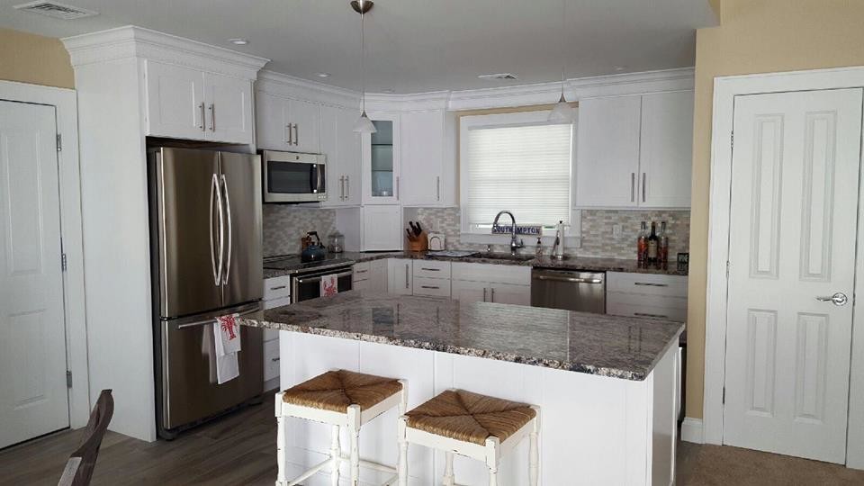 Eat-in kitchen - mid-sized coastal l-shaped ceramic tile eat-in kitchen idea in New York with an undermount sink, shaker cabinets, white cabinets, granite countertops, beige backsplash, glass sheet backsplash, stainless steel appliances and an island
