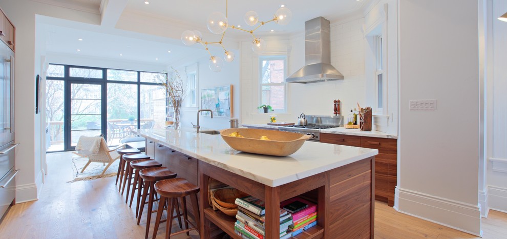 Photo of a large urban galley kitchen/diner in Toronto with a submerged sink, flat-panel cabinets, medium wood cabinets, marble worktops, white splashback, ceramic splashback, stainless steel appliances, light hardwood flooring and an island.
