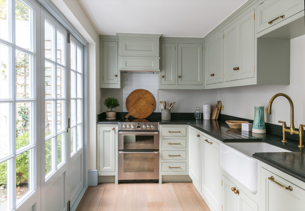 Foto på ett litet, avskilt vintage l-kök, med en rustik diskho, luckor med infälld panel, gröna skåp, granitbänkskiva, vitt stänkskydd, stänkskydd i keramik, beiget golv, rostfria vitvaror och ljust trägolv