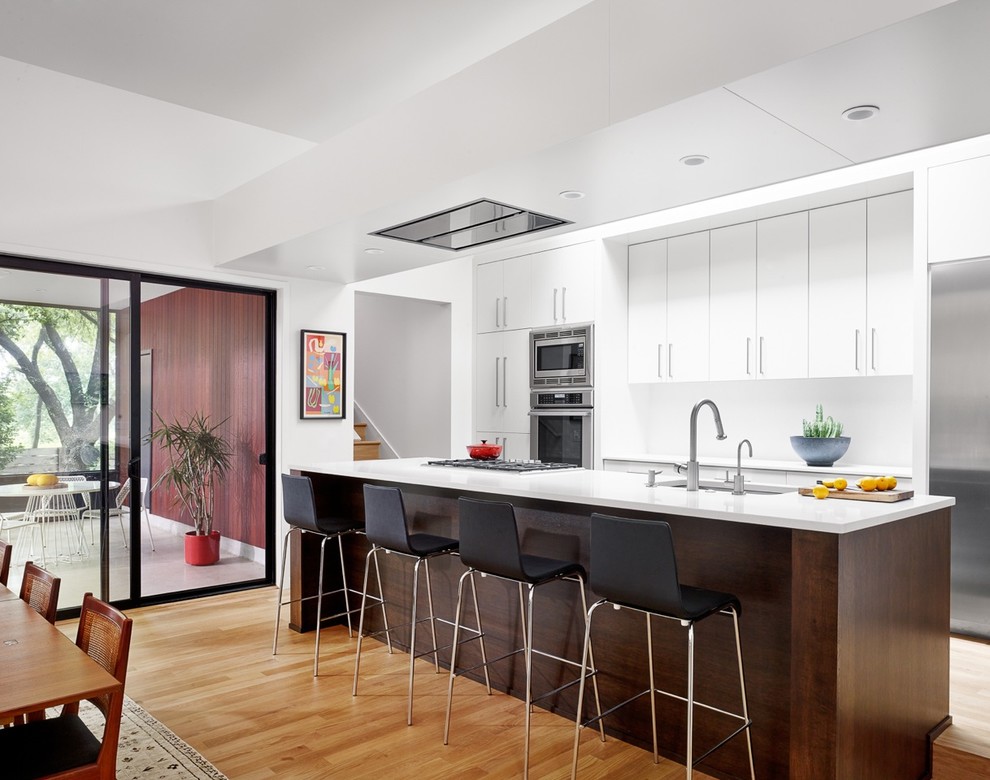 Foto di una cucina design con lavello sottopiano, ante lisce, ante bianche, elettrodomestici in acciaio inossidabile e parquet chiaro