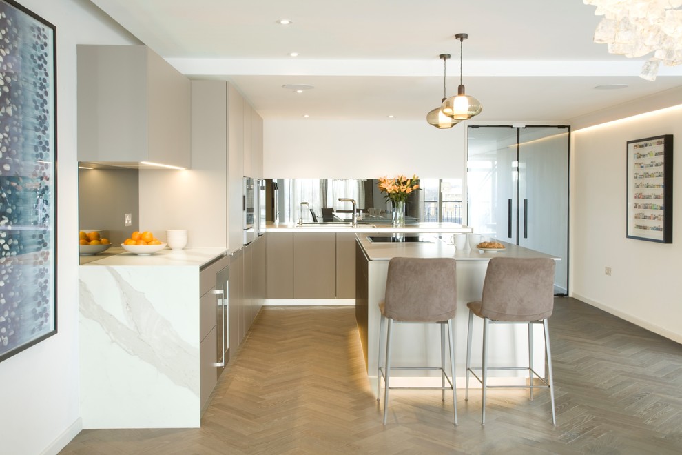 Inspiration for a medium sized contemporary l-shaped kitchen in London with a submerged sink, flat-panel cabinets, grey cabinets, marble worktops, mirror splashback, stainless steel appliances, light hardwood flooring, an island and beige floors.
