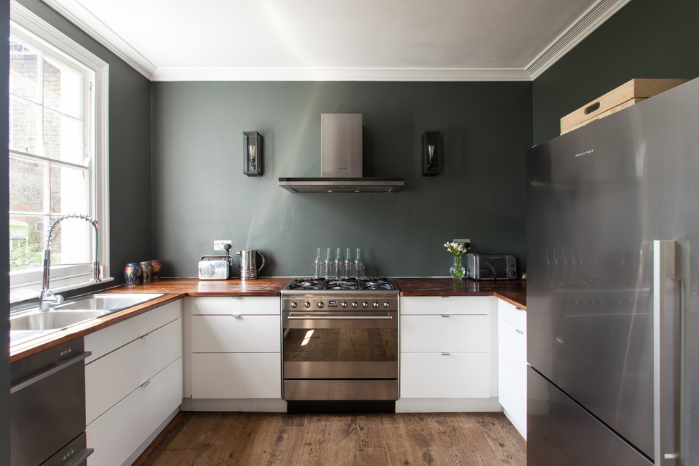 This is an example of a contemporary u-shaped kitchen in London with a double-bowl sink, flat-panel cabinets, white cabinets, wood worktops, stainless steel appliances, medium hardwood flooring, brown floors and brown worktops.