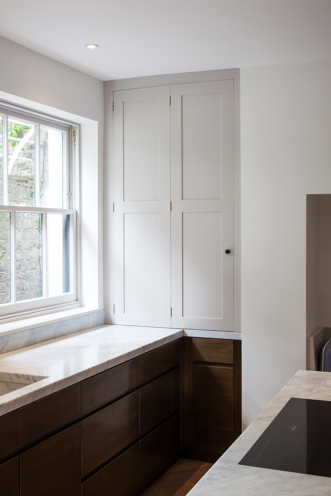 Photo of a large contemporary l-shaped open plan kitchen in London with recessed-panel cabinets, distressed cabinets, marble worktops, grey splashback, marble splashback, stainless steel appliances, light hardwood flooring, an island, brown floors, grey worktops and a built-in sink.