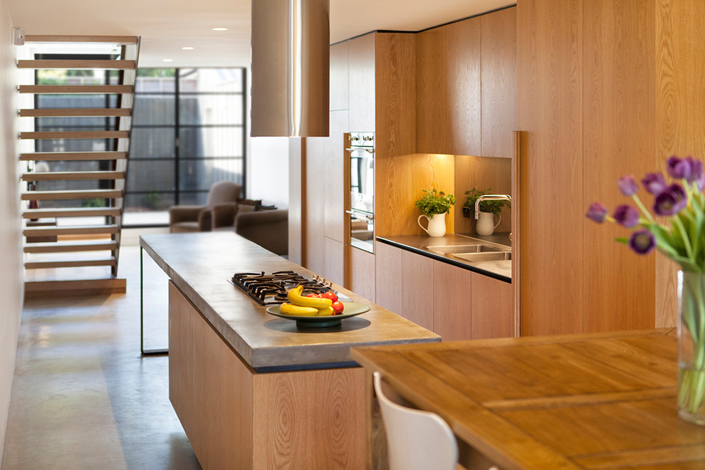 Esempio di una cucina minimalista con lavello a doppia vasca, ante lisce, ante in legno chiaro, top in cemento, paraspruzzi con lastra di vetro, elettrodomestici in acciaio inossidabile e pavimento in cemento