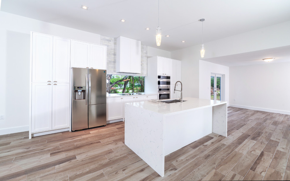 Foto på ett mellanstort funkis vit linjärt kök med öppen planlösning, med en undermonterad diskho, skåp i shakerstil, vita skåp, marmorbänkskiva, fönster som stänkskydd, rostfria vitvaror, mellanmörkt trägolv, en köksö och brunt golv