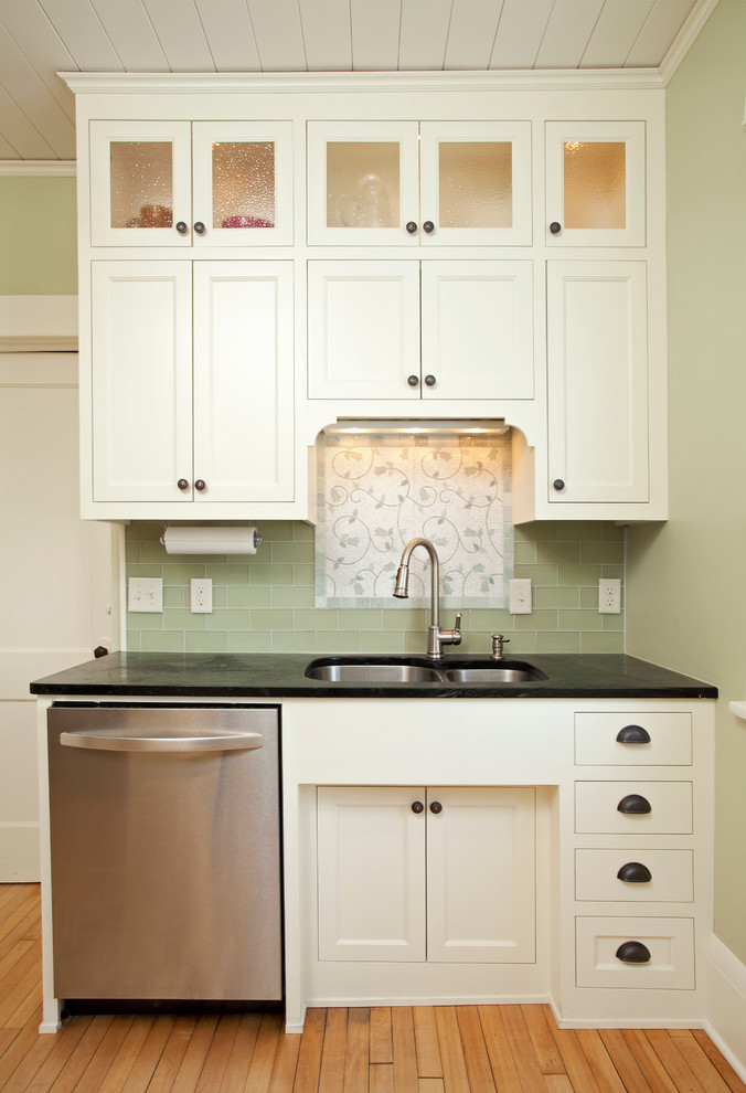 Example of a small classic light wood floor and beige floor enclosed kitchen design in Minneapolis with an undermount sink, recessed-panel cabinets, white cabinets, soapstone countertops, green backsplash, glass tile backsplash, stainless steel appliances and no island