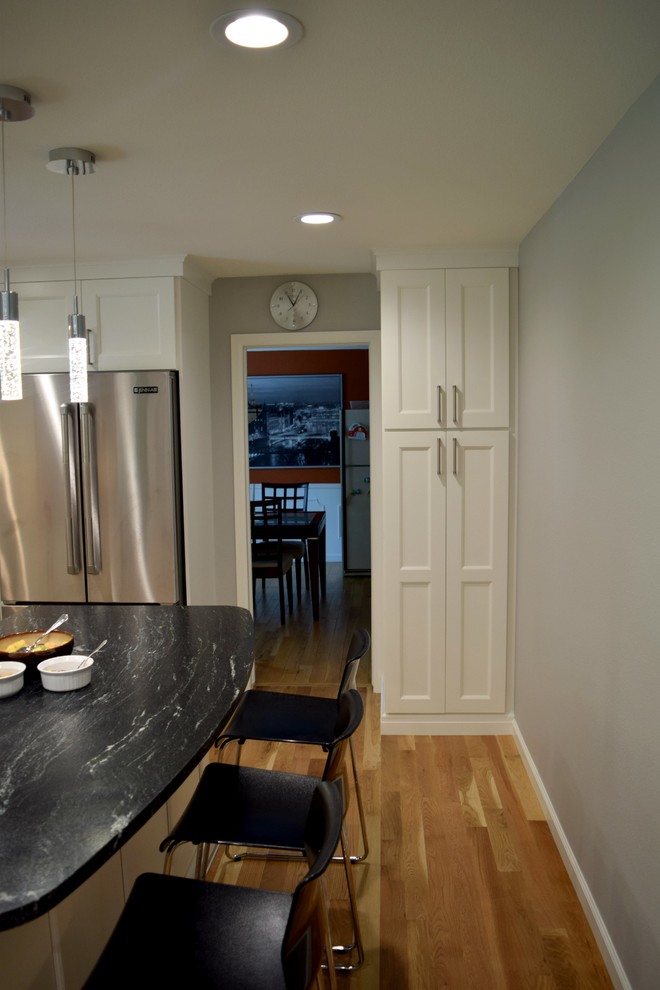 This is an example of a contemporary l-shaped kitchen/diner in Denver with a submerged sink, flat-panel cabinets, white cabinets, granite worktops, white splashback, glass tiled splashback, stainless steel appliances, medium hardwood flooring and an island.