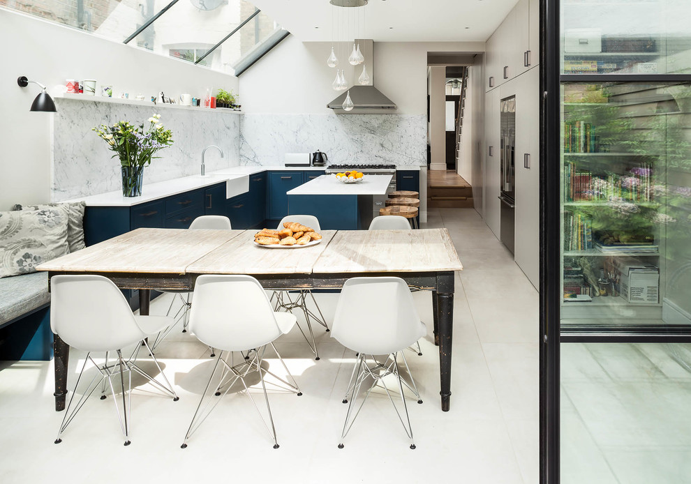 Photo of a medium sized contemporary u-shaped kitchen/diner in London with porcelain flooring, a belfast sink, flat-panel cabinets, blue cabinets, marble worktops, white splashback, marble splashback, an island and white floors.