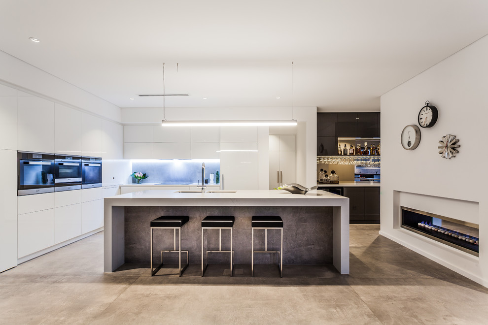 На фото: угловая кухня-гостиная в современном стиле с плоскими фасадами, белыми фасадами, бетонным полом и островом с