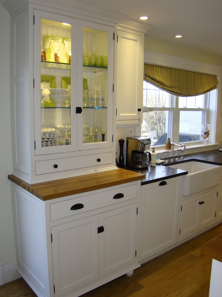 This is an example of a small contemporary l-shaped open plan kitchen in Portland Maine with a belfast sink, beaded cabinets, white cabinets, wood worktops, white splashback, metro tiled splashback, stainless steel appliances, medium hardwood flooring and an island.