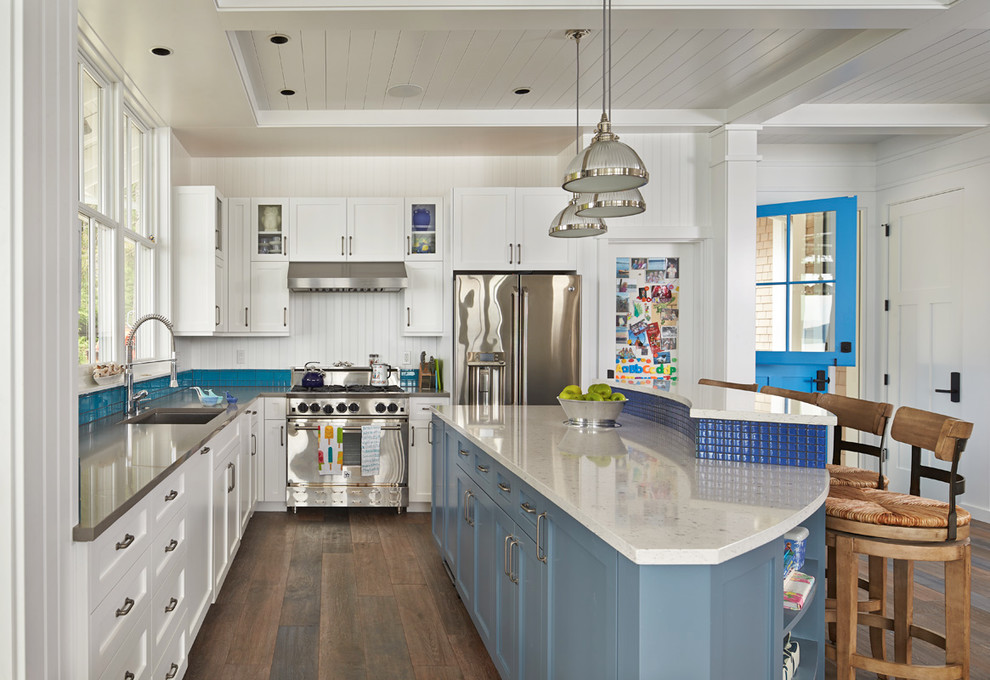 На фото: кухня в морском стиле с врезной мойкой, фасадами в стиле шейкер, белыми фасадами, синим фартуком, техникой из нержавеющей стали, темным паркетным полом, островом и окном