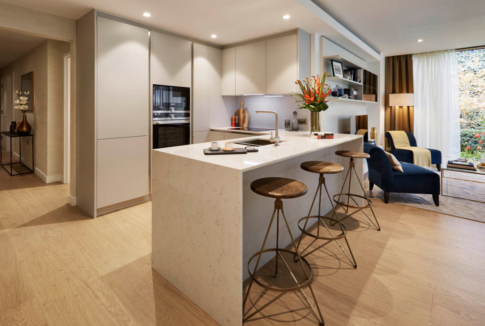Photo of a contemporary u-shaped open plan kitchen in London with flat-panel cabinets, grey cabinets, engineered stone countertops, black appliances, white worktops, a double-bowl sink, light hardwood flooring, a breakfast bar and beige floors.