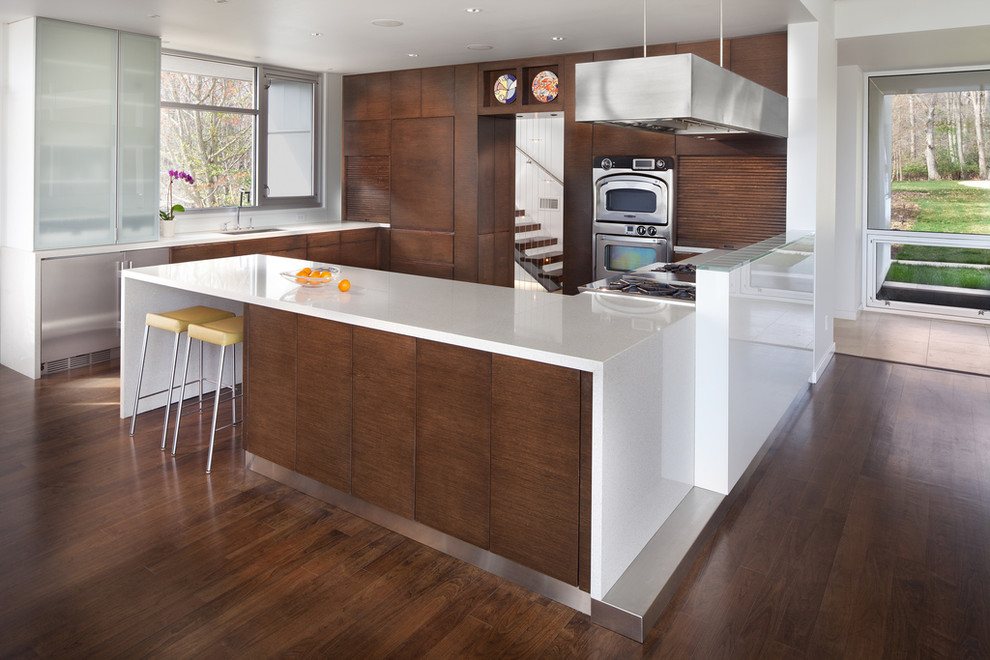 Example of a large l-shaped dark wood floor kitchen pantry design in DC Metro with a drop-in sink, flat-panel cabinets, medium tone wood cabinets, solid surface countertops, stainless steel appliances and no island