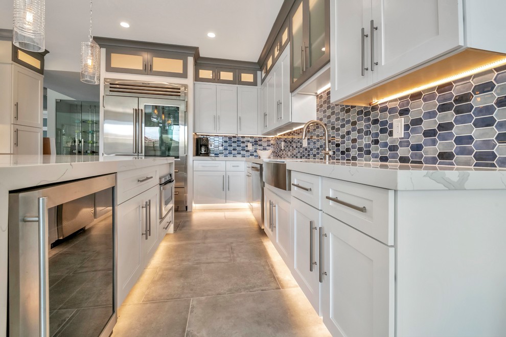 Inspiration for a large coastal u-shaped porcelain tile and gray floor eat-in kitchen remodel in Phoenix with a farmhouse sink, shaker cabinets, white cabinets, quartz countertops, blue backsplash, glass tile backsplash, stainless steel appliances, an island and white countertops