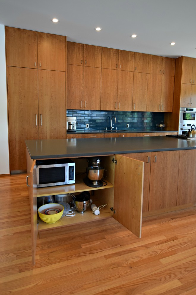 Exemple d'une très grande cuisine ouverte linéaire moderne en bois brun avec un évier encastré, un placard à porte plane, une crédence noire, un électroménager en acier inoxydable, un sol en bois brun et îlot.