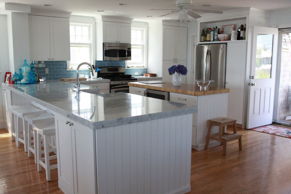 Inspiration for a large coastal u-shaped kitchen/diner in Boston with a belfast sink, shaker cabinets, white cabinets, engineered stone countertops, blue splashback, metro tiled splashback, stainless steel appliances, light hardwood flooring, an island and brown floors.