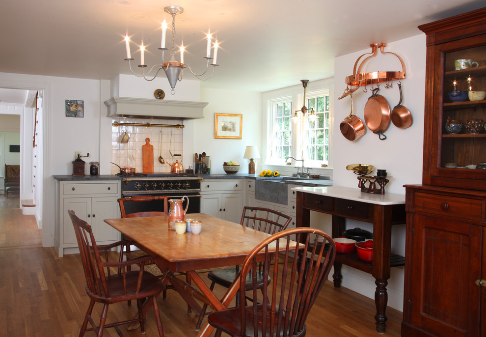 Example of a mid-sized cottage l-shaped medium tone wood floor and brown floor eat-in kitchen design in Boston with a farmhouse sink, recessed-panel cabinets, green cabinets, soapstone countertops, beige backsplash, ceramic backsplash, black appliances and no island