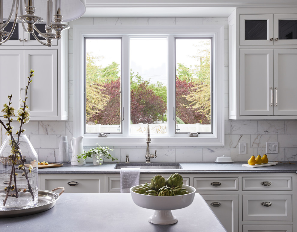 Inspiration för mellanstora klassiska grått kök, med en undermonterad diskho, luckor med profilerade fronter, vita skåp, bänkskiva i kvarts, vitt stänkskydd, stänkskydd i marmor, rostfria vitvaror, kalkstensgolv, en köksö och grått golv