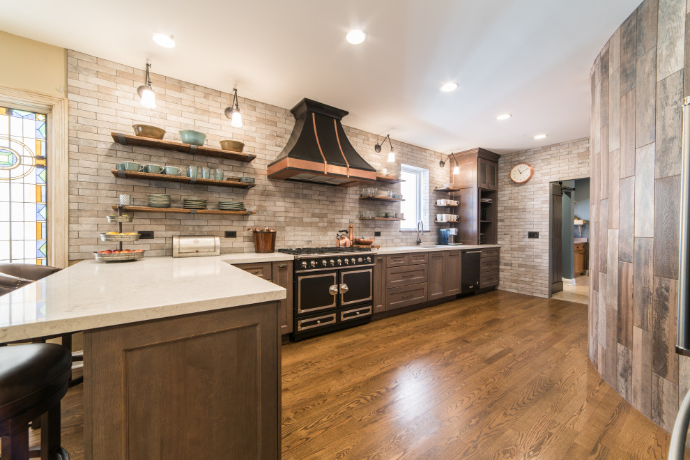 Inspiration for a rustic l-shaped dark wood floor and brown floor kitchen remodel in Chicago with a peninsula, an undermount sink, shaker cabinets, dark wood cabinets, gray backsplash, black appliances and white countertops
