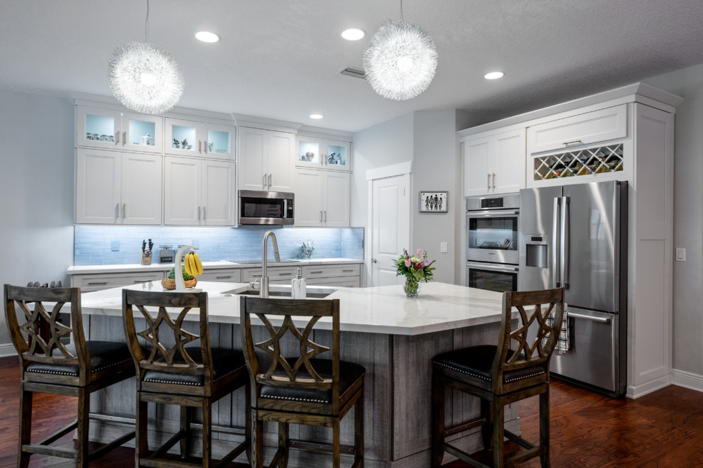 Inspiration for a mid-sized transitional l-shaped medium tone wood floor and brown floor eat-in kitchen remodel in Tampa with an undermount sink, shaker cabinets, white cabinets, tile countertops, gray backsplash, subway tile backsplash, black appliances, an island and white countertops