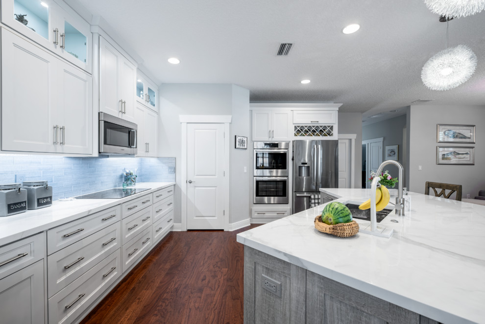 Inspiration for a mid-sized transitional l-shaped medium tone wood floor and brown floor eat-in kitchen remodel in Tampa with an undermount sink, shaker cabinets, white cabinets, tile countertops, gray backsplash, subway tile backsplash, black appliances, an island and white countertops