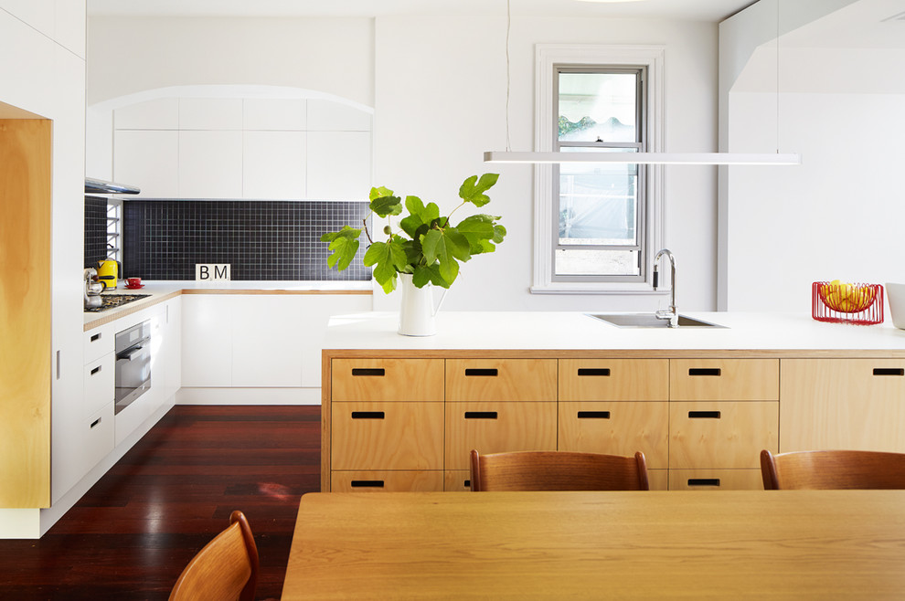 Inredning av ett modernt litet kök, med en enkel diskho, släta luckor, vita skåp, svart stänkskydd, stänkskydd i mosaik, rostfria vitvaror, mörkt trägolv och en köksö