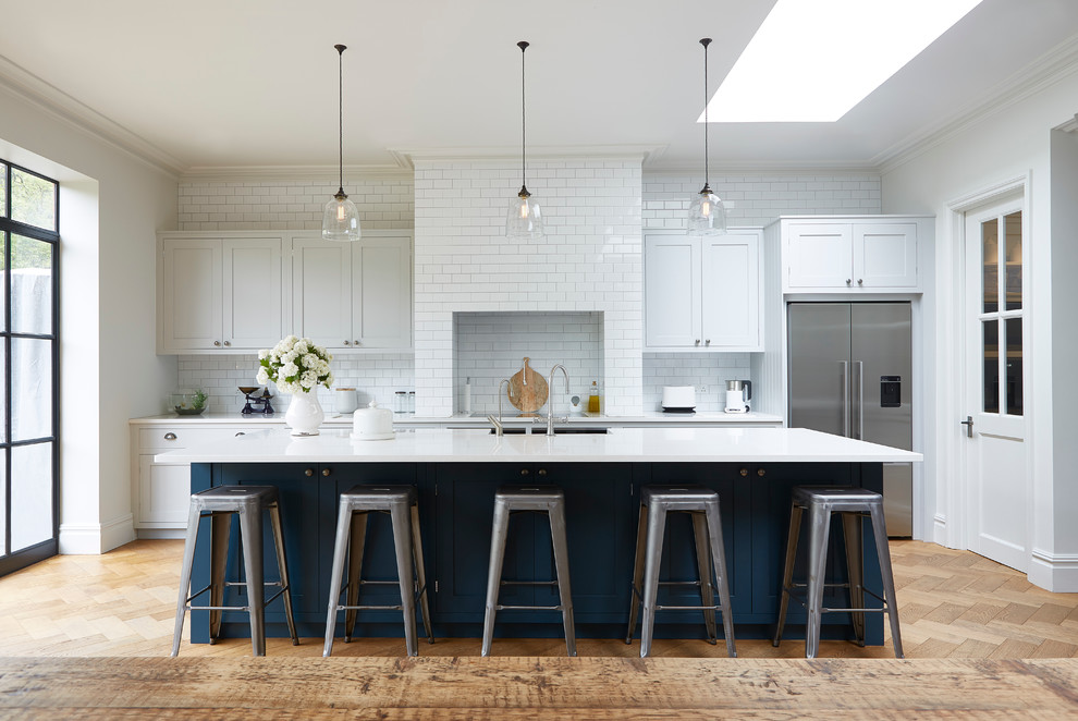 Transitional galley medium tone wood floor kitchen photo in London with shaker cabinets, white cabinets, white backsplash, subway tile backsplash, stainless steel appliances and an island