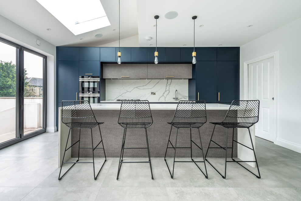 Modern inredning av ett mellanstort vit linjärt vitt kök med öppen planlösning, med en enkel diskho, släta luckor, blå skåp, bänkskiva i kvartsit, vitt stänkskydd, stänkskydd i marmor, rostfria vitvaror, cementgolv, en köksö och grått golv