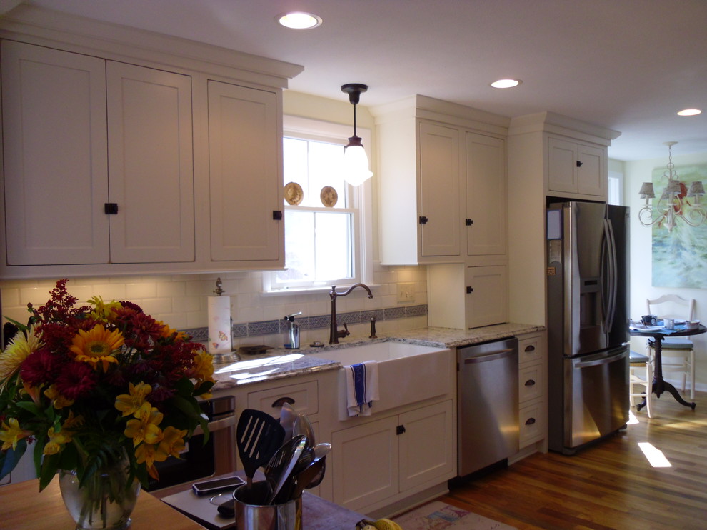 Foto på ett avskilt, stort lantligt vit linjärt kök, med en rustik diskho, skåp i shakerstil, vita skåp, granitbänkskiva, vitt stänkskydd, stänkskydd i tunnelbanekakel, rostfria vitvaror, mörkt trägolv, en köksö och brunt golv