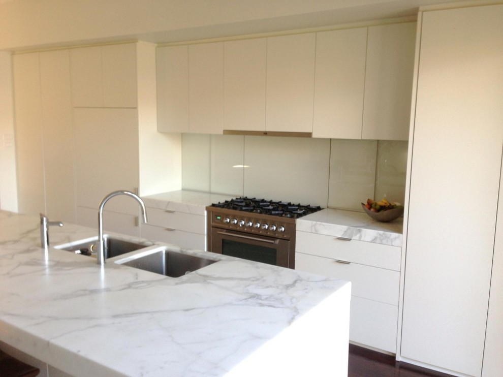 Zweizeilige Moderne Küche mit flächenbündigen Schrankfronten, weißen Schränken, Marmor-Arbeitsplatte, Küchenrückwand in Weiß, Glasrückwand, Küchengeräten aus Edelstahl und Kücheninsel in Melbourne