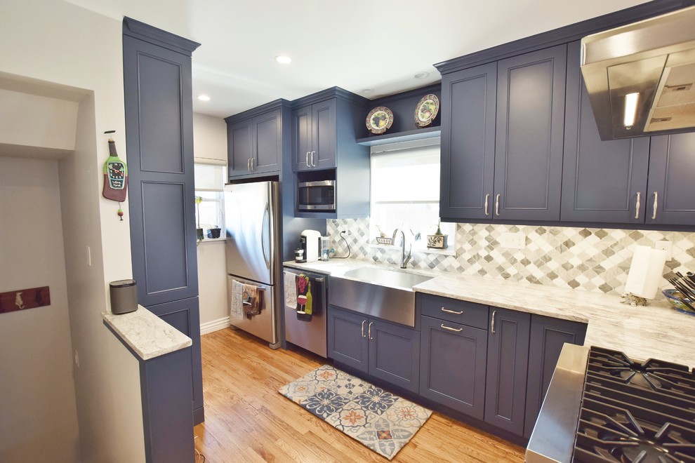 Inredning av ett klassiskt litet kök, med en rustik diskho, luckor med infälld panel, blå skåp, grått stänkskydd, rostfria vitvaror och mellanmörkt trägolv