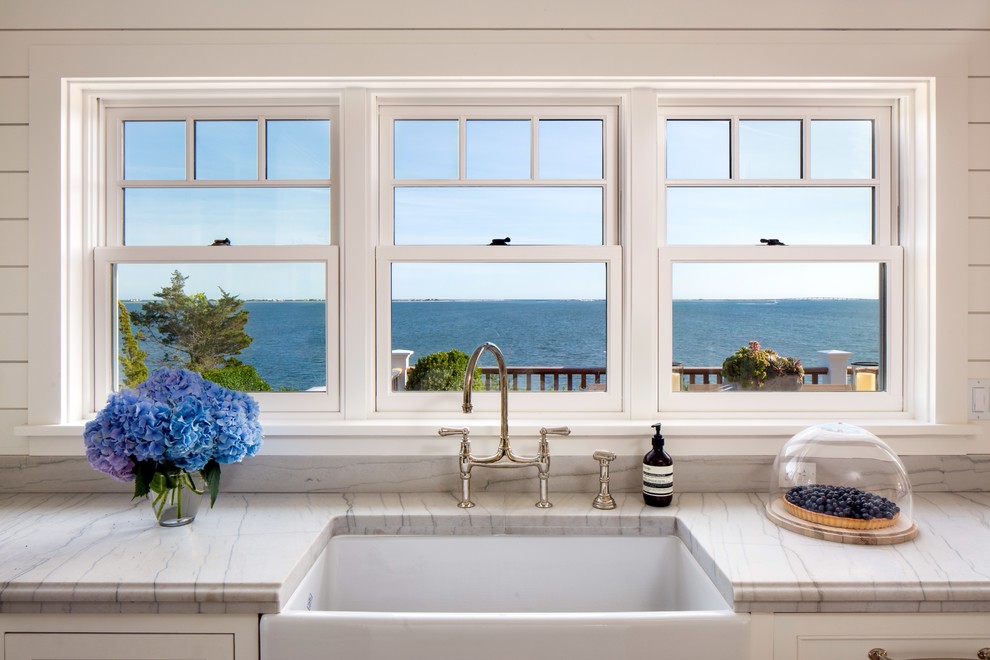 Coastal u-shaped enclosed kitchen in New York with glass-front cabinets, white cabinets, white splashback, stainless steel appliances and an island.