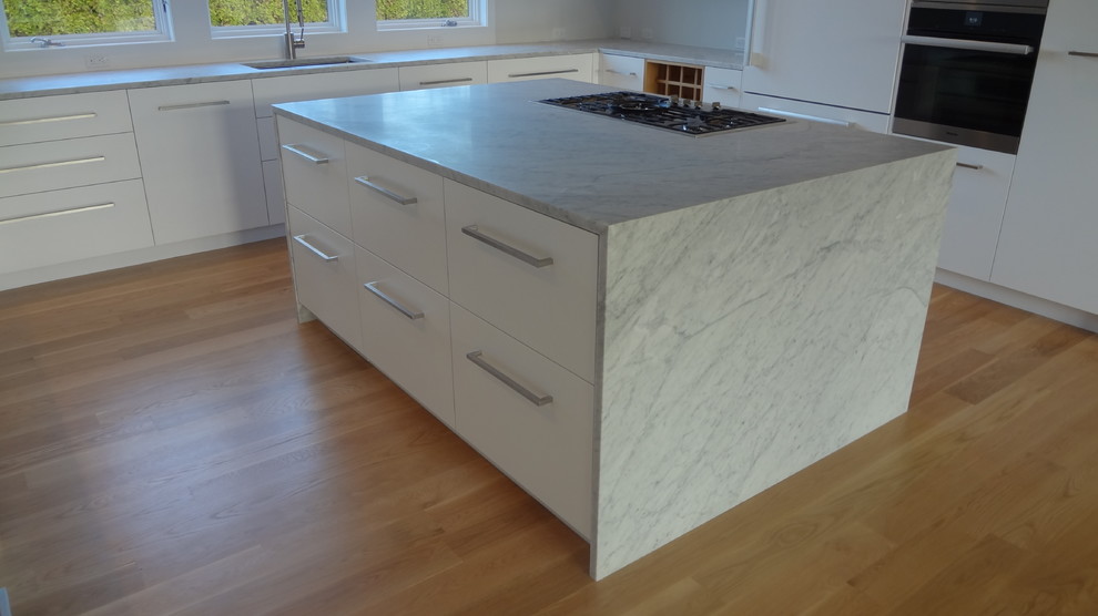 Immagine di una grande cucina minimalista con lavello sottopiano, ante lisce, ante bianche, top in marmo e parquet chiaro