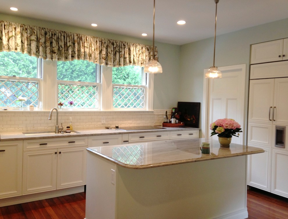 Example of a mid-sized classic l-shaped medium tone wood floor and brown floor eat-in kitchen design in Boston with an undermount sink, recessed-panel cabinets, beige cabinets, quartzite countertops, beige backsplash, subway tile backsplash, paneled appliances and an island