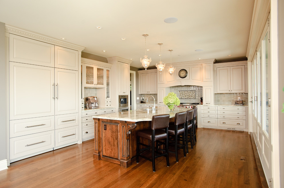 Klassisk inredning av ett l-kök, med luckor med upphöjd panel, vita skåp, grått stänkskydd och integrerade vitvaror
