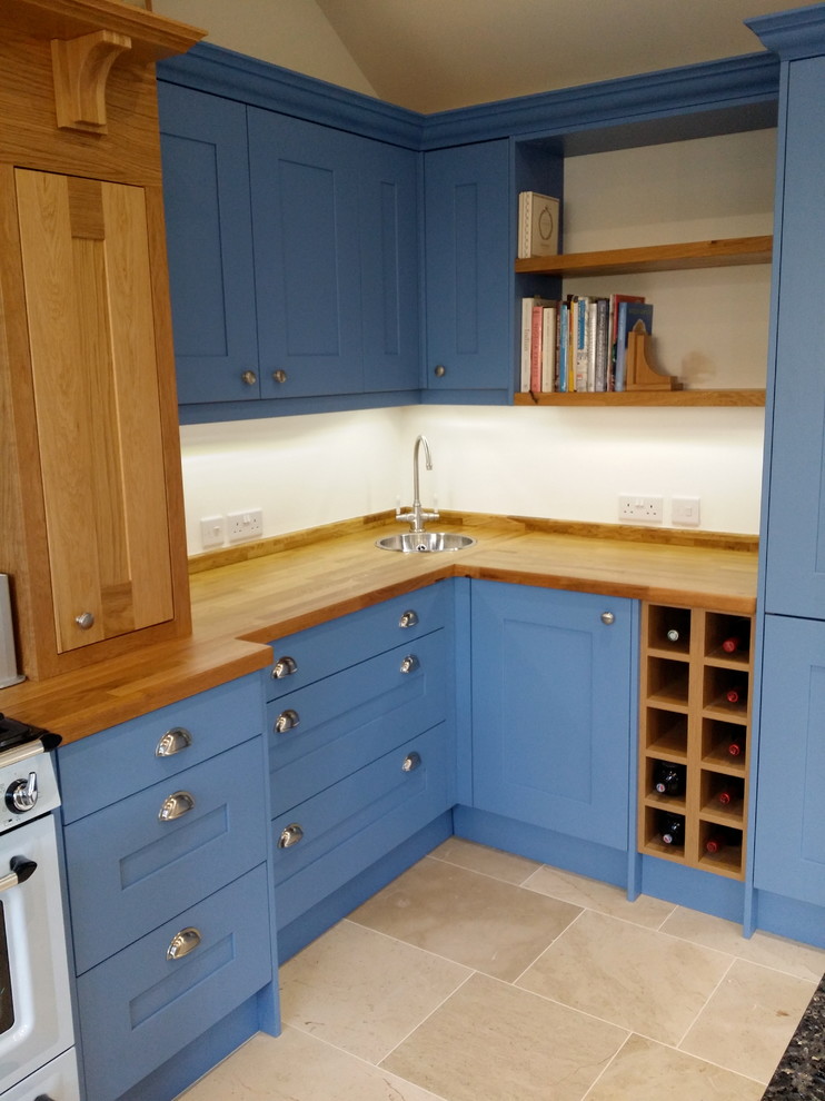 Cette image montre une cuisine traditionnelle avec un évier 1 bac, des portes de placard bleues, un plan de travail en bois, un sol en travertin et un sol beige.