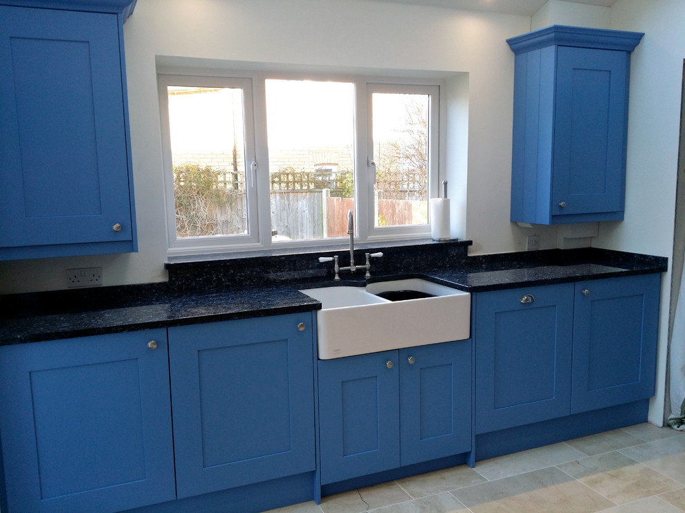 Klassische Küche mit Landhausspüle, blauen Schränken, Granit-Arbeitsplatte, weißen Elektrogeräten, Travertin und beigem Boden in Dorset