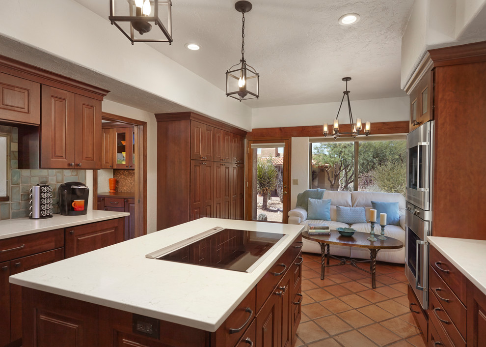 Exempel på ett stort klassiskt kök, med en undermonterad diskho, luckor med upphöjd panel, bruna skåp, bänkskiva i kvarts, blått stänkskydd, stänkskydd i glaskakel, rostfria vitvaror, klinkergolv i terrakotta, en köksö och brunt golv