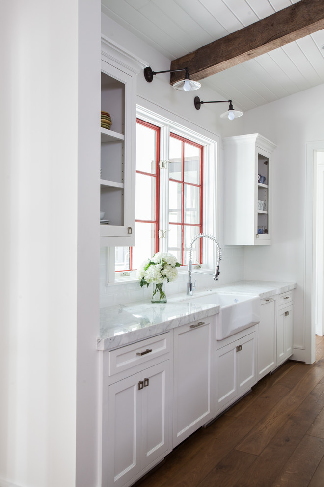 Modelo de cocina tradicional renovada con puertas de armario blancas, fregadero sobremueble, armarios estilo shaker, salpicadero blanco y suelo de madera oscura