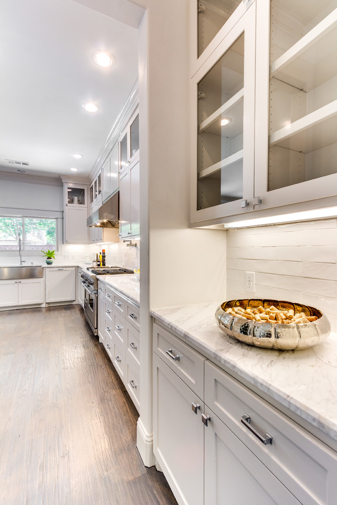 Inspiration for a transitional medium tone wood floor kitchen remodel in Dallas with a farmhouse sink, shaker cabinets, white cabinets, marble countertops, white backsplash, porcelain backsplash and stainless steel appliances