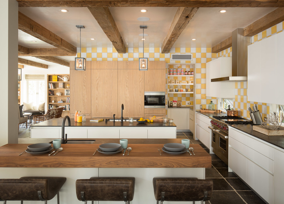Пример оригинального дизайна: кухня-гостиная в современном стиле с врезной мойкой, плоскими фасадами, белыми фасадами, желтым фартуком и техникой под мебельный фасад