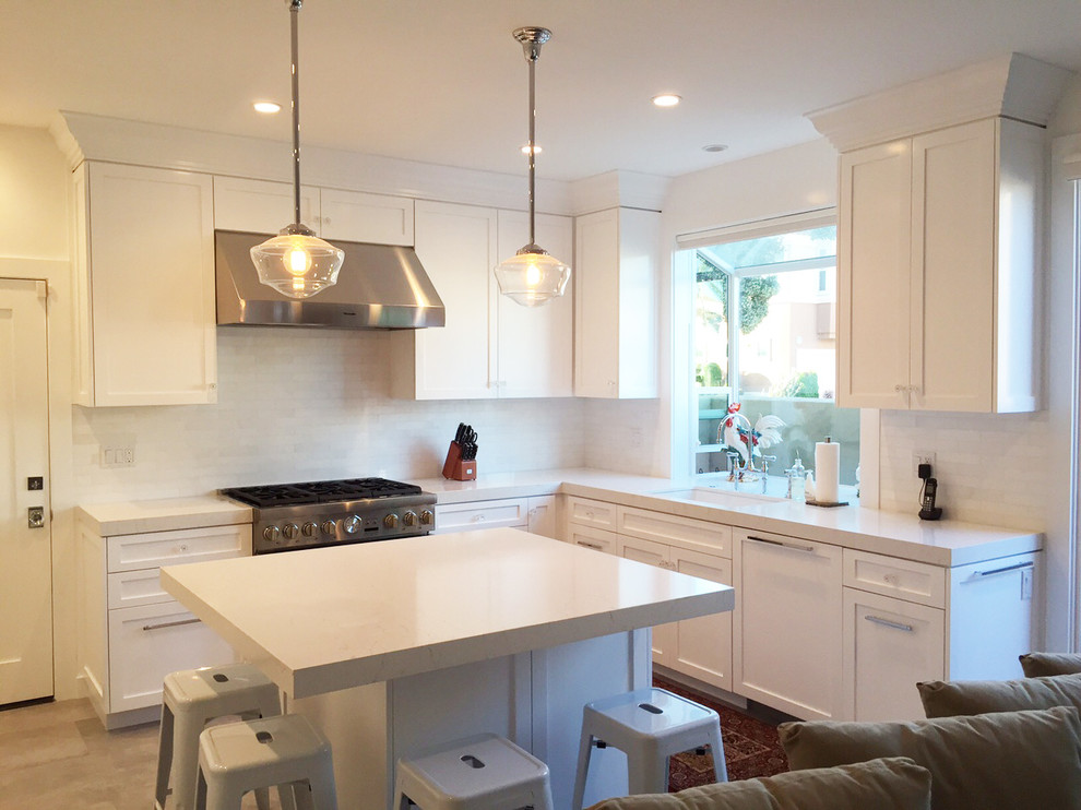 This is an example of a medium sized beach style l-shaped open plan kitchen in Huntington with a single-bowl sink, shaker cabinets, white cabinets, engineered stone countertops, white splashback, ceramic splashback, stainless steel appliances, porcelain flooring and an island.