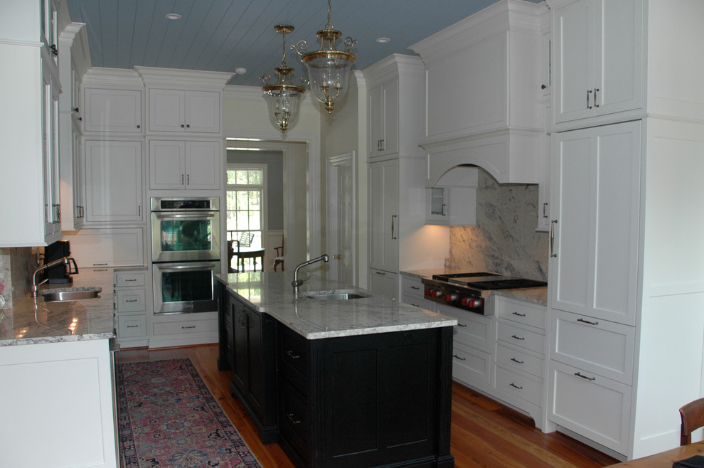 Bild på ett vintage kök, med en undermonterad diskho, luckor med profilerade fronter, vita skåp, bänkskiva i kvartsit, stänkskydd i sten, integrerade vitvaror, mellanmörkt trägolv och en köksö