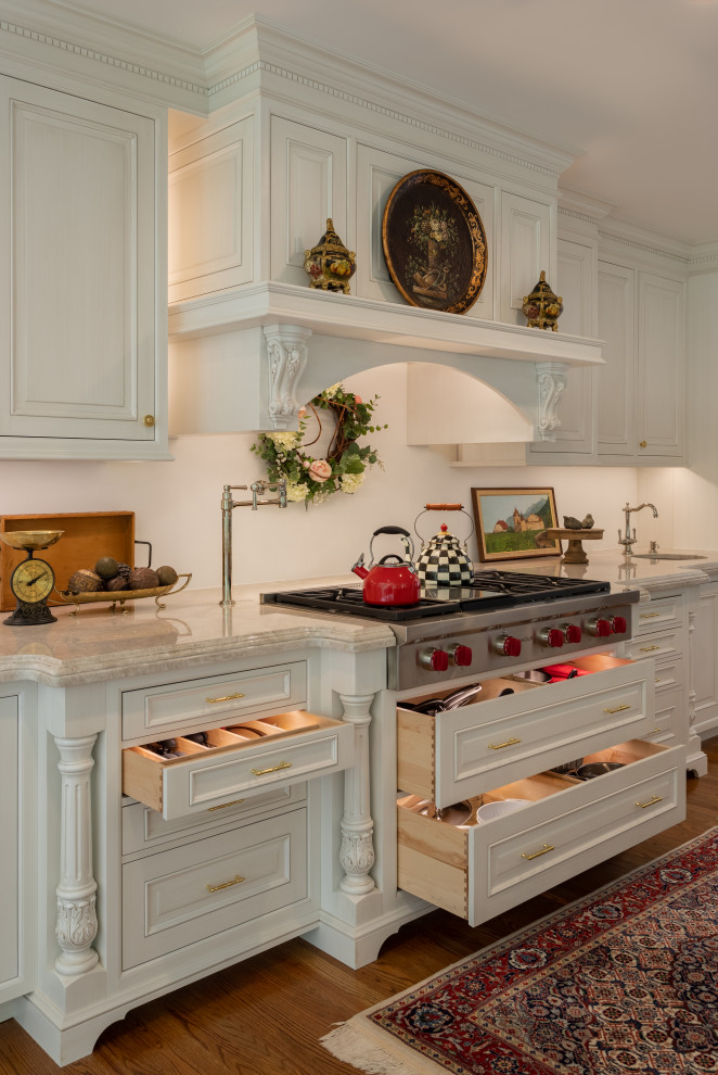 Inredning av ett klassiskt mycket stort vit vitt kök, med luckor med upphöjd panel, vita skåp, bänkskiva i kvartsit, vitt stänkskydd, mellanmörkt trägolv, en köksö och brunt golv