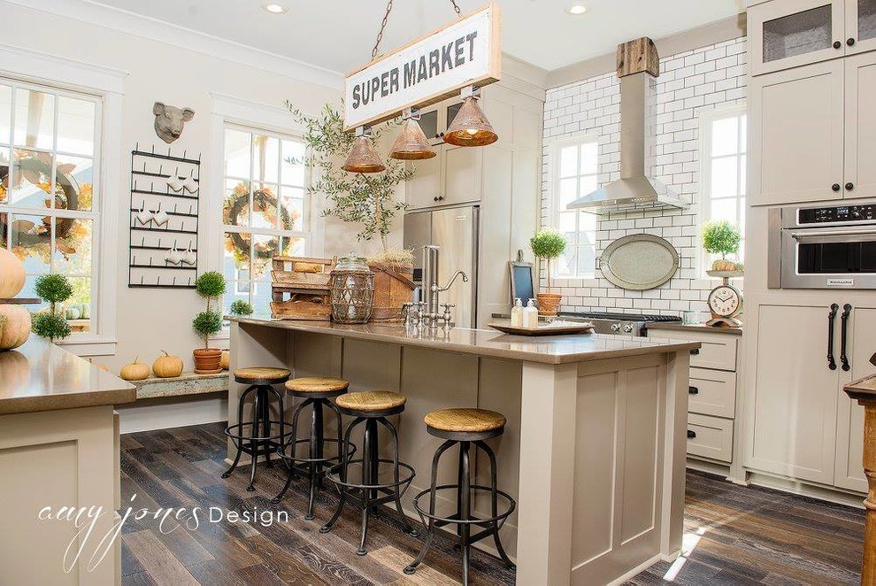 Mid-sized country medium tone wood floor enclosed kitchen photo in Little Rock with a farmhouse sink, shaker cabinets, gray cabinets, quartz countertops, white backsplash, subway tile backsplash, stainless steel appliances and an island