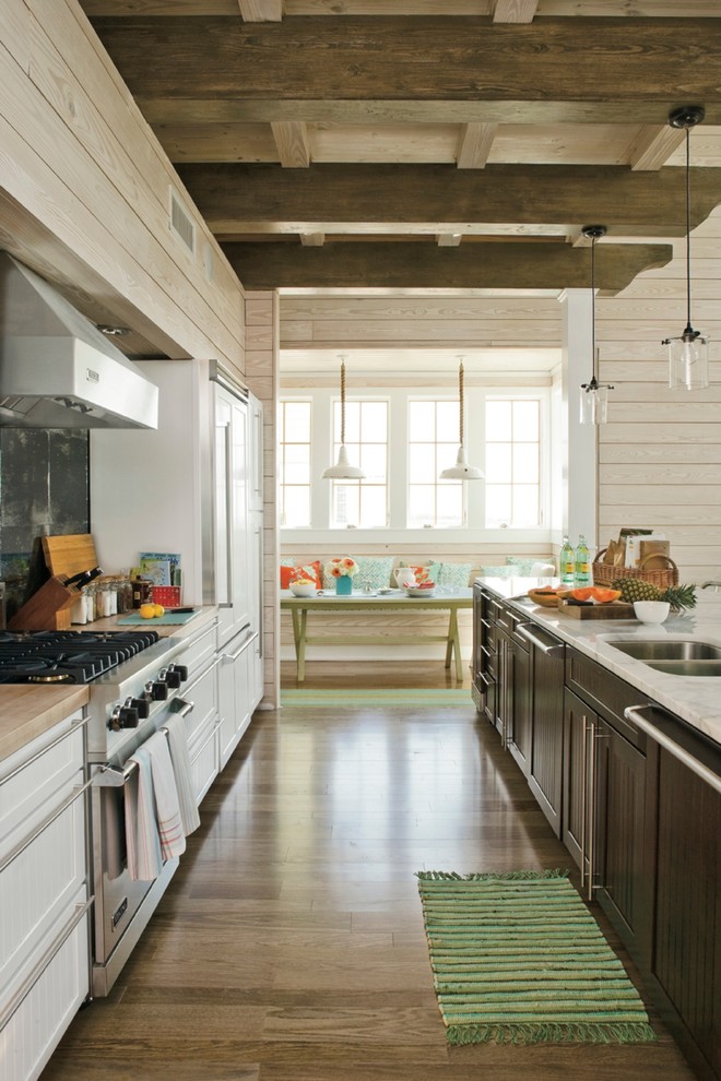 Exemple d'une cuisine américaine parallèle bord de mer avec un évier 2 bacs, un placard avec porte à panneau encastré, des portes de placard blanches, un électroménager en acier inoxydable, un sol en bois brun et îlot.