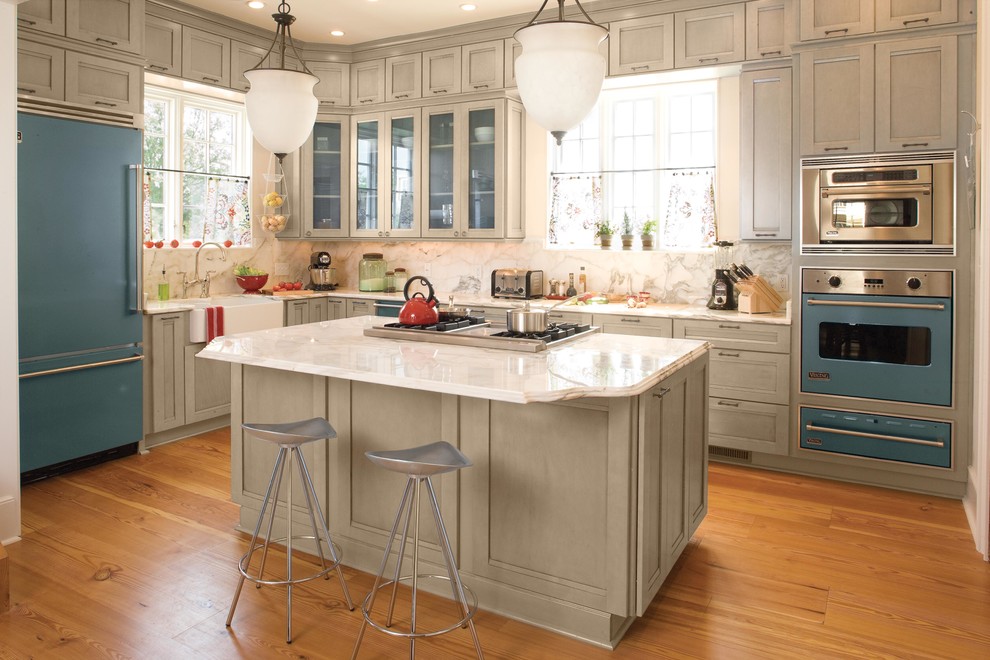 Photo of a nautical galley kitchen/diner in Birmingham with a belfast sink, recessed-panel cabinets, white cabinets, coloured appliances, medium hardwood flooring, an island, white splashback and stone slab splashback.