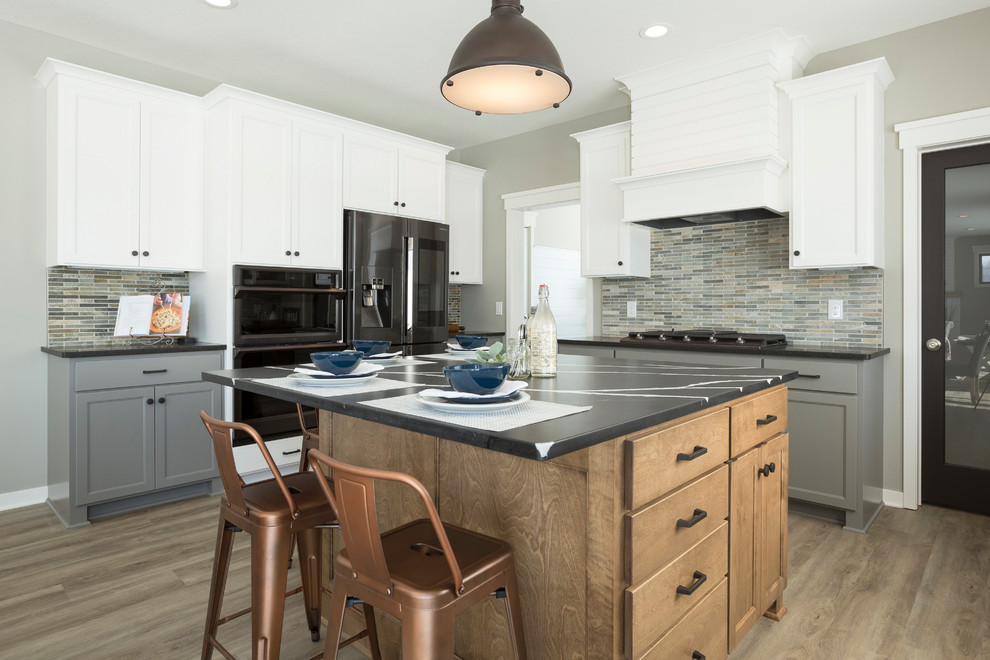 This is an example of a traditional grey and white kitchen in Minneapolis with shaker cabinets, white cabinets, multi-coloured splashback, matchstick tiled splashback, black appliances, dark hardwood flooring, an island, brown floors and black worktops.