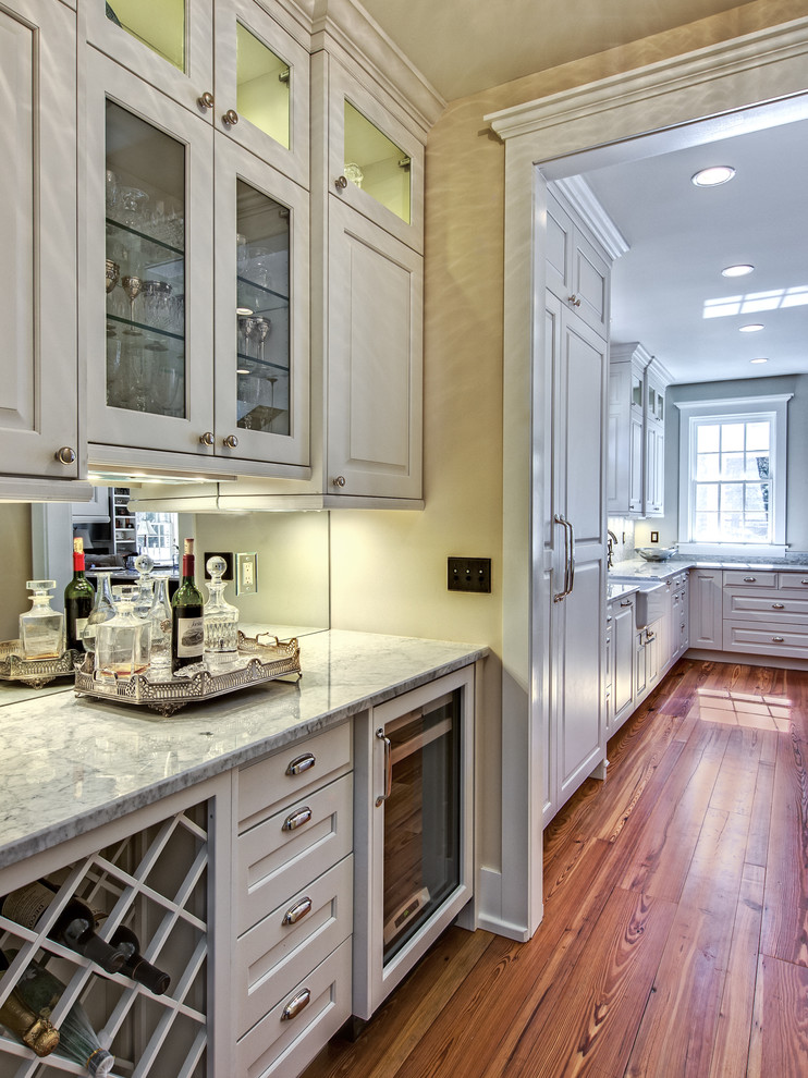 Example of a huge classic light wood floor kitchen design in Denver with a farmhouse sink, raised-panel cabinets, white cabinets, marble countertops, paneled appliances and an island